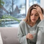 How does a painkiller really “know” where it hurts? Woman holding a glass of water with hand on forehead