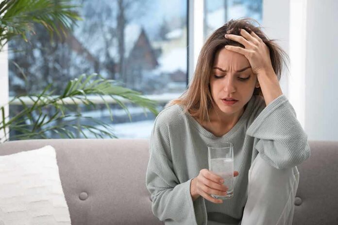 Woman holding a glass of water with hand on forehead