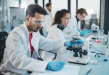 College Duo Stuns America With Cancer Hack Scientist using a microscope in a modern laboratory