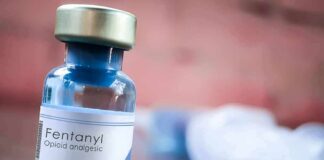 Fentanyl vial on a table with blurred syringe in background