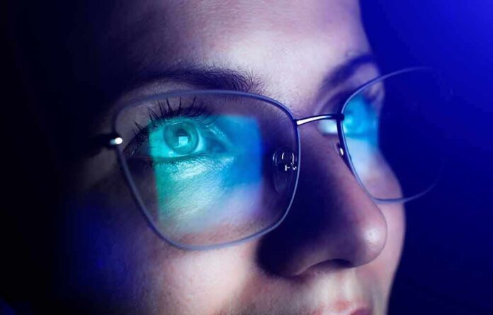 Person wearing glasses with blue light reflecting on lenses