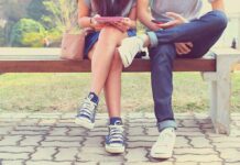 Two people sitting on a park bench using mobile devices