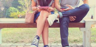 Two people sitting on a park bench using mobile devices