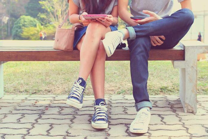 Two people sitting on a park bench using mobile devices